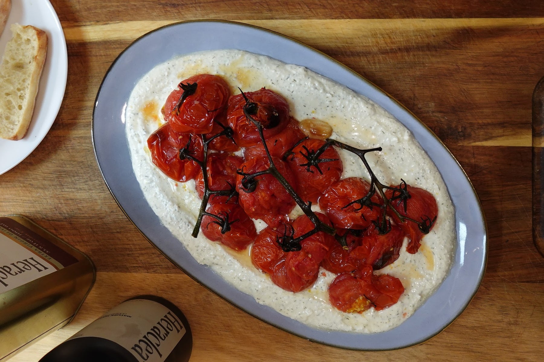 Whipped feta dip in a shallow bowl topped with jammy olive oil roasted cherry tomatoes, garlic, and pooling golden olive oil