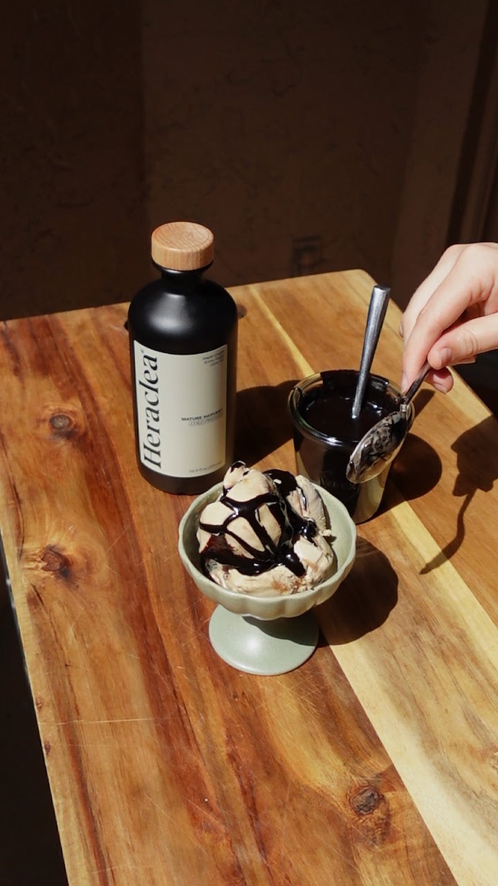 Glossy olive oil hot fudge sauce being poured over vanilla ice cream in a sundae glass