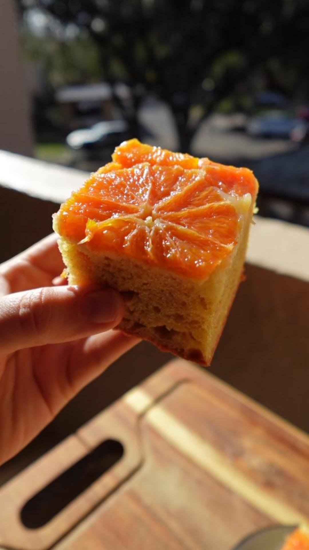 Slice of upside-down orange olive oil cake held up to the light, topped with a caramelized Cara Cara orange round