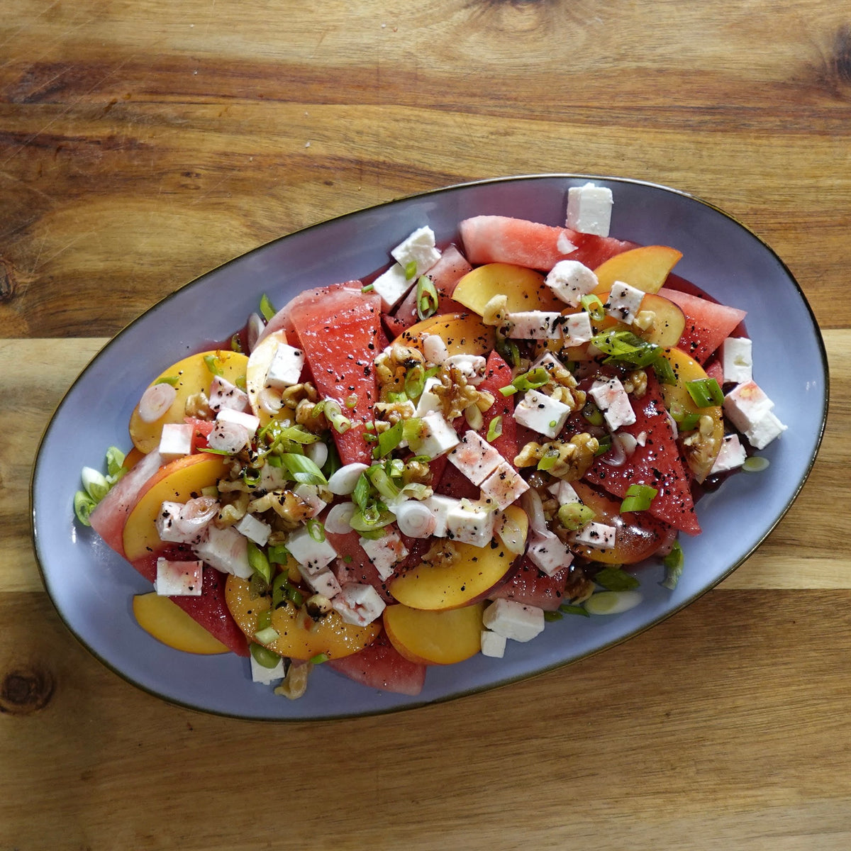 Watermelon feta salad with nectarines, walnuts, and green onions on an oval platter