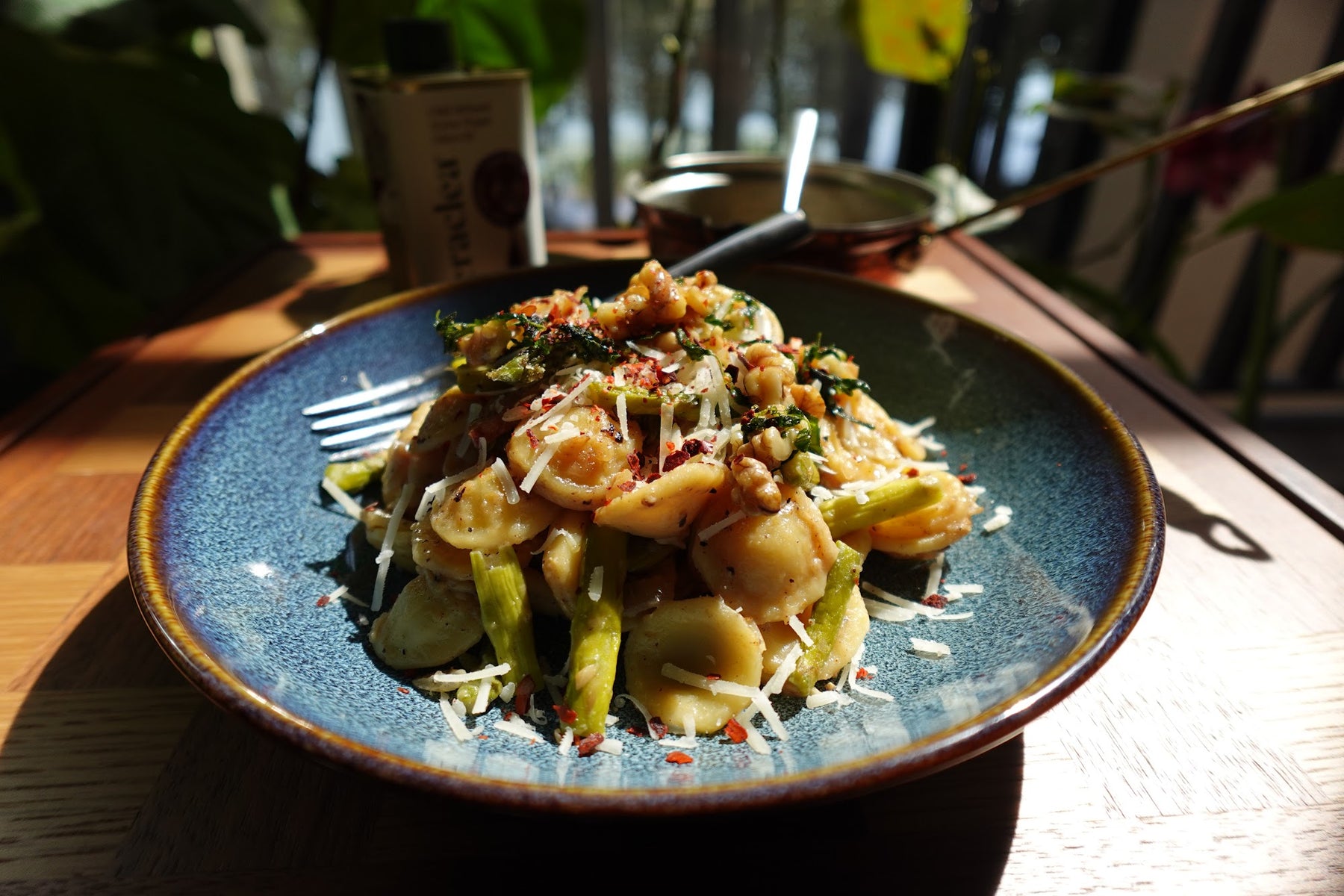Asparagus and bacon orecchiette topped with toasted walnuts and chili olive oil, served in a blue ceramic bowl