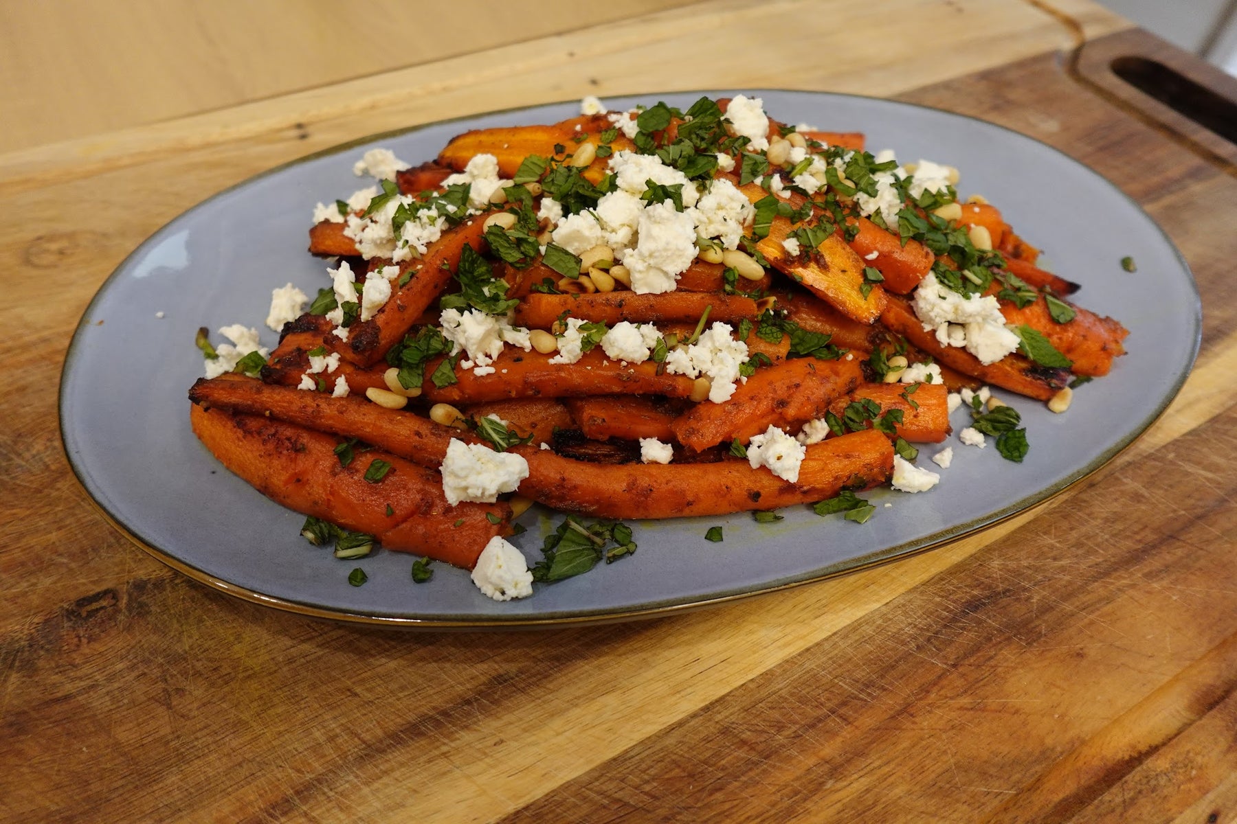 Hawaij-spiced olive oil roasted carrots on a platter topped with crumbled feta, fresh mint, and toasted pine nuts