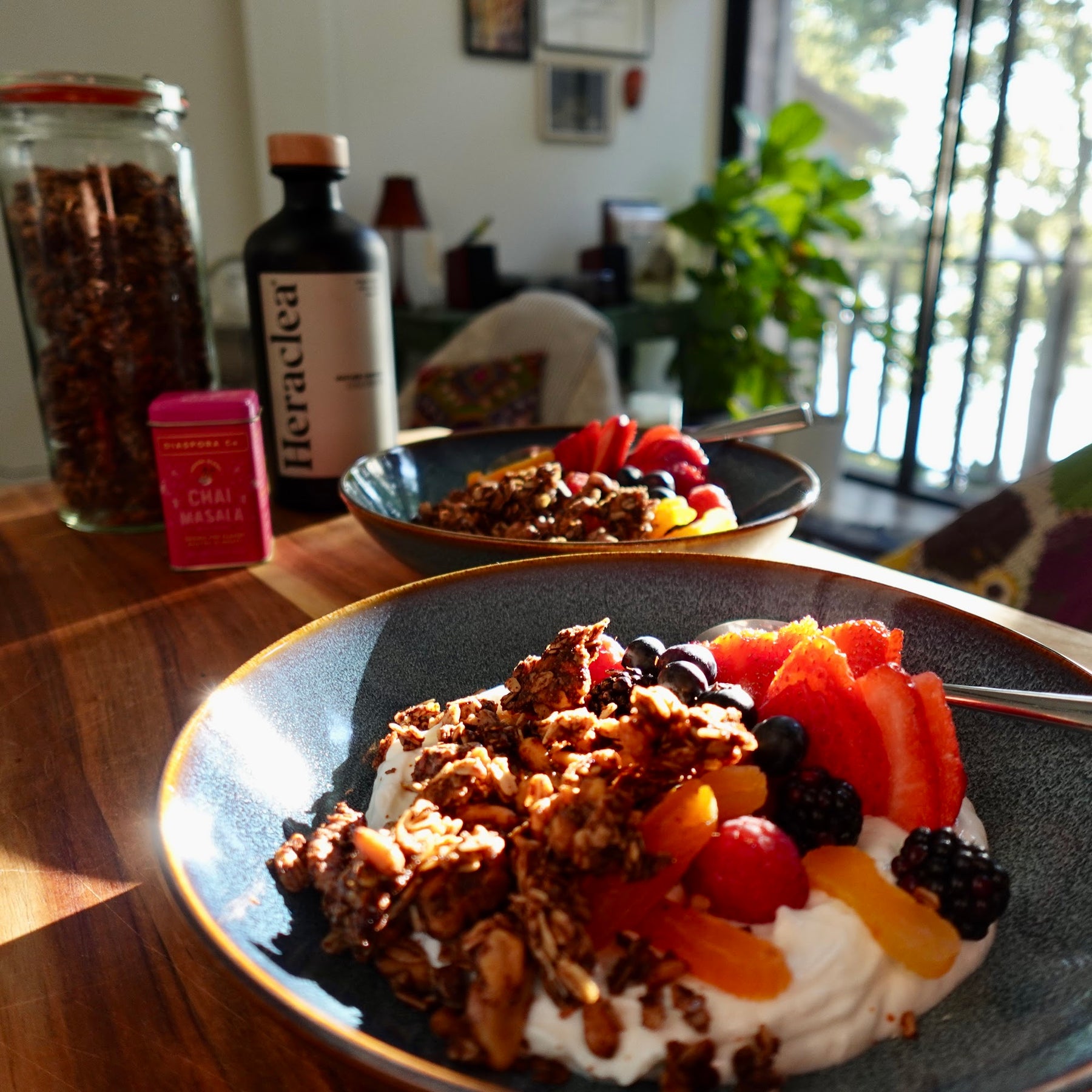 Chai-spiced olive oil granola served over yogurt with strawberries, blueberries, blackberries, and dried apricots, with a Heraclea olive oil bottle in the background