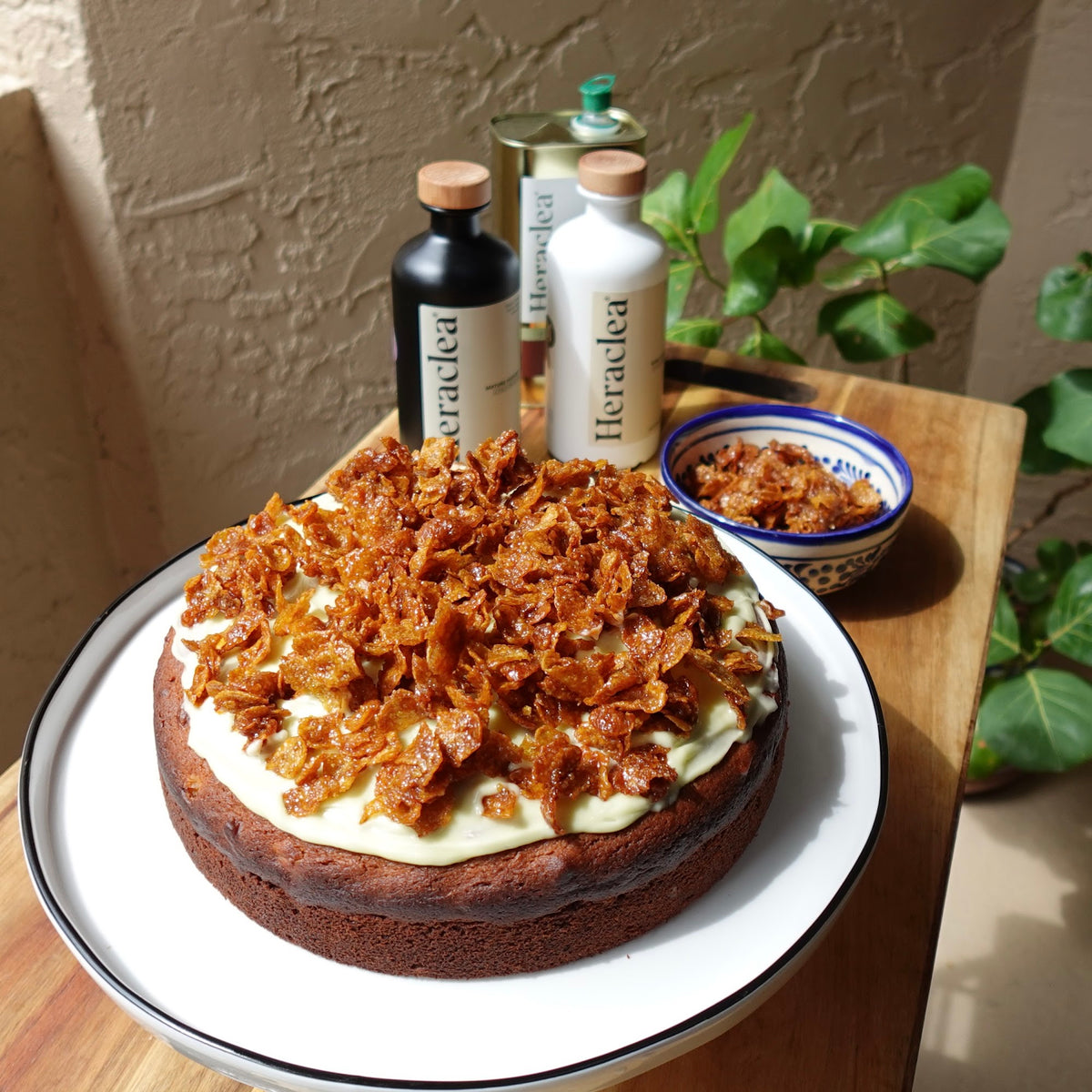 Golden sweet corn and olive oil cake topped with candied corn flakes, with Heraclea olive oil bottles behind