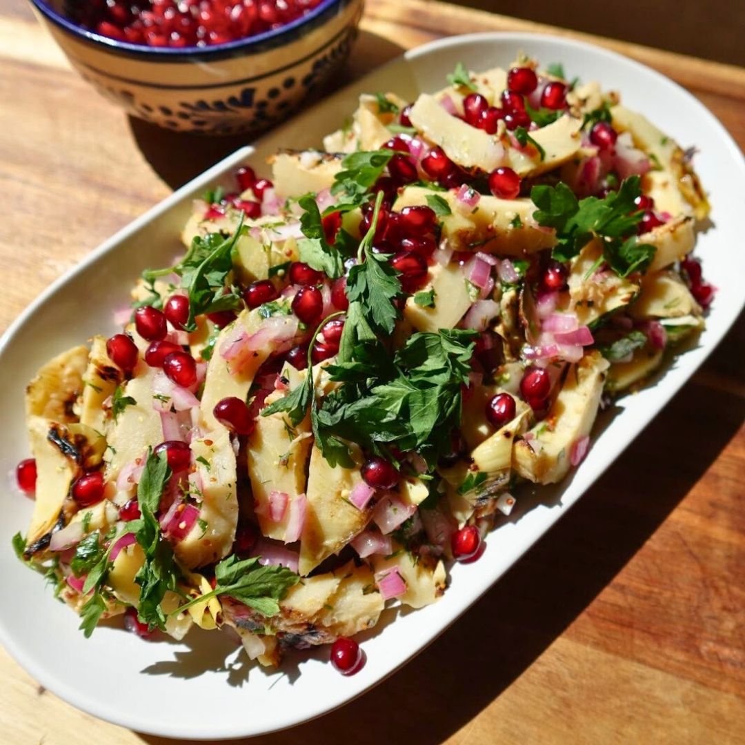 Charred artichoke salad with pomegranate seeds and fresh herbs on an oval platter